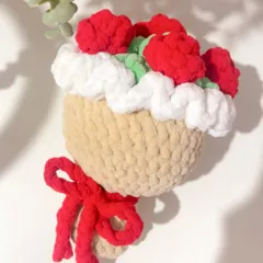 A close-up shot of my rose plush bouquet hanging as a decorative piece. The design features red roses and a fluffy white border, all crocheted from soft, thick yarn and tied with a red bow.