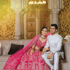 This is a perfect example of coordinated styling for a modern reception or engagement. The bride's vibrant pink lehenga is intricately detailed, and the groom's elegant white sherwani provides a beautiful contrast, creating a look that is both regal and contemporary.