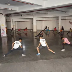 Students perform deep lunging stretches as part of their warm-up routine. Flexibility is crucial for preventing injuries and executing powerful fencing movements.