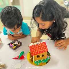 A mother and her two little boys work together to decorate their gingerbread house with colorful candies and icing.