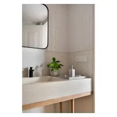 A close-up of a cast in-situ white terrazzo sink resting on a simple rubberwood base. The contrast between the smooth, speckled terrazzo and the vertical lines of the subway tiles behind it creates a subtle textural dialogue.