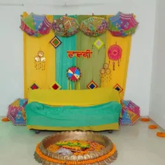A simple and colorful Haldi setup for an intimate ceremony. The decor uses yellow and green drapes, decorative umbrellas, and a traditional 'urli' in the front.