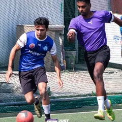 Two players challenge for the ball in a competitive 5-a-side game. The enclosed, netted turf ensures the action is continuous and exciting.