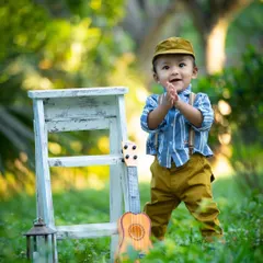 Clapping with joy in the great outdoors. This little boy's happiness is palpable in this sunny, green setting, complete with a miniature guitar for a musical touch.