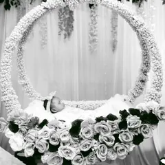 An artistic black and white photograph of a newborn sleeping peacefully in a custom-designed circular floral cradle, a highlight of my naming ceremony photography and decor service.