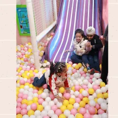 Three children at the bottom of our slide, surrounded by a sea of pink, yellow, and white balls. The ball pit is one of our most popular attractions.