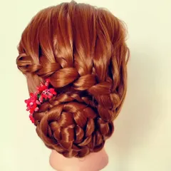 A complex braided bun with interwoven sections, decorated with bright red floral accessories. This style is a statement piece for any traditional event.