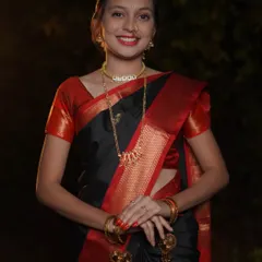A direct and engaging portrait for Makar Sankrant. The subject looks straight at the camera with a warm smile, showcasing her traditional black saree and gold jewelry against a softly lit background.