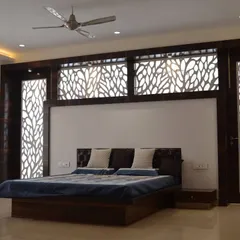 This spacious master bedroom features an elaborate custom headboard wall with integrated, backlit jaali panels in a nature-inspired pattern. The dark wood finish and clean lines of the bed frame create a look of contemporary elegance.