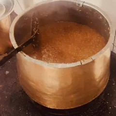 Sakkarai Pongal, a sweet rice dish made with jaggery, being slow-cooked in a large brass vessel. This traditional method ensures even cooking and a richer taste.