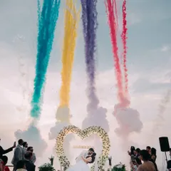 The climax of a beach wedding ceremony, with vibrant smoke effects creating a magical atmosphere against the evening sky.