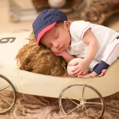 A future baseball star. This baby is dressed in a mini baseball uniform, sleeping in a vintage-style toy car and holding a baseball.