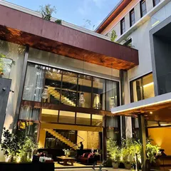 The interior of this Koramangala home, seen through the floor-to-ceiling windows, reveals a floating staircase and modern chandeliers, showcasing our approach to luxury interiors.