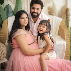 A happy family maternity portrait in a boho-chic studio setting. The expecting mother, father, and their daughter smile together, capturing the excitement of waiting for the new arrival.