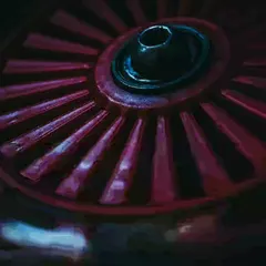 A close-up of a red industrial wheel. The dark, moody lighting and intense color create a powerful and abstract image from a mechanical object.