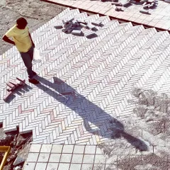 The timeless herringbone pattern is used here for a paved area, with the long shadow of a worker adding a dramatic, graphic quality. This work-in-progress shot highlights the beauty of pattern and precision in hardscape design.