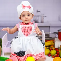Our little chef is ready to cook up some fun. Dressed in a chef's hat and apron, she's surrounded by fresh fruits in our kitchen-themed setup.