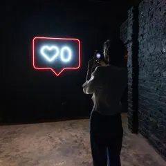 Another angle of a person engaging with the 'Heart 0' neon sign. The dark, industrial setting of the gallery space enhances the impact of the glowing light.