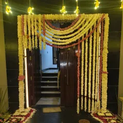 A traditional and elaborate floral entrance decoration for a home Diwali puja. The entire door frame is covered in garlands of white and pink flowers, with flower petal rangoli at the base.