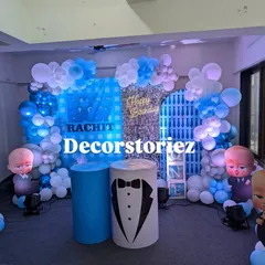 A closer look at the Boss Baby themed decor, highlighting the custom backdrop with the child's name, the tuxedo-themed pedestal, and the detailed balloon work in shades of blue and white.