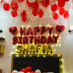 I can personalize your birthday decorations with a name, like this 'SHAFIA' foil balloon setup. The 'Happy Birthday' letters are complemented by the name in gold, with red and white balloons filling the room.