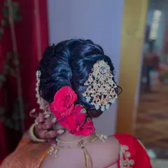 This is a classic bridal khopa, elevated with deep red roses and an ornate jeweled accessory. I build the bun to be full and balanced, ensuring it looks perfect from every angle and securely holds the weight of the flowers and jewelry. This style is a statement of pure bridal opulence.