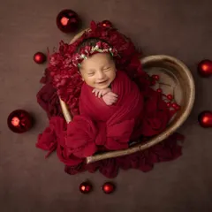 A beautiful smile from a newborn nestled in a heart shaped bowl, surrounded by festive red ornaments. This is the perfect way to celebrate your baby's first holiday season.