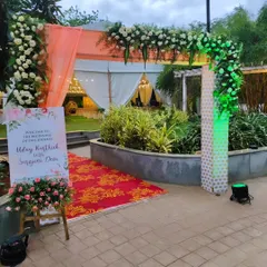 An outdoor entrance arch for a corporate event, combining a fabric canopy with white and green floral arrangements. The custom welcome sign adds a personal touch for guests.
