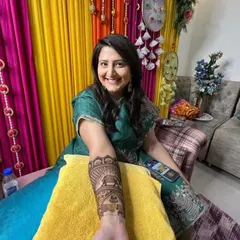 A smiling client proudly displaying her arm mehandi. The design features traditional elephant and floral motifs, perfect for her celebration.