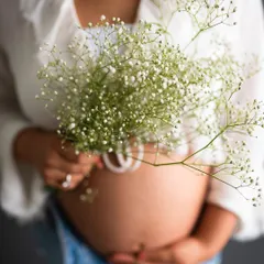 A beautiful close-up focusing on the baby bump, with the delicate baby's breath flowers adding a soft, sweet touch.