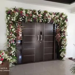 A grand floral entrance decoration for a housewarming ceremony. We framed the main door with a lush arch of fresh flowers, including roses, carnations, and heliconia, to create a stunning welcome for guests.