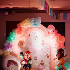 A fun photo backdrop with a rainbow balloon arch and clown and lion props. The wallpaper features cute, subtle circus animal illustrations.