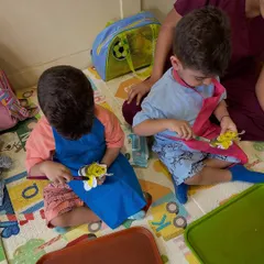 Two little boys completely focused on their bee-themed craft. They are using paintbrushes to add yellow and black stripes to their paper bees.