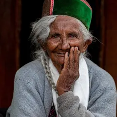 The joyful, wrinkled face of an elderly woman in a traditional Himachali cap. Her smile is infectious and holds the wisdom of a life lived in the mountains.