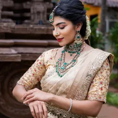 This elegant cream and gold tissue silk saree is paired with emerald jewelry for a stunning contrast. It's a sophisticated choice for a wedding reception or engagement, offering a regal and timeless appeal.