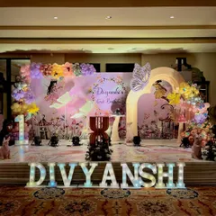 Here is a full stage setup for an enchanted butterfly themed first birthday. The design includes a custom backdrop with fairy silhouettes, large marquee letters for the child's name, and elegant balloon garlands to create a magical atmosphere.