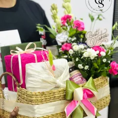 A large, impressive gift basket being held, ready for delivery. It's overflowing with fresh tuberoses and pink flowers, beautifully wrapped gifts, and a "Best Wishes" sign, perfect for any major celebration.