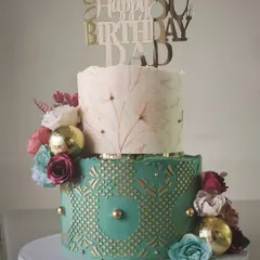 A distinguished two-tiered cake for an 80th birthday. The design includes a hand-painted floral top tier and a bottom tier with a green and gold geometric pattern, creating a look of timeless elegance.