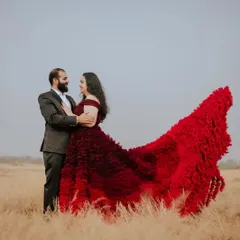 This couple is sharing a sweet look in a beautiful open field. The dramatic red ruffled train of her gown spreads out in the grass, adding a pop of color and romance to the natural landscape.