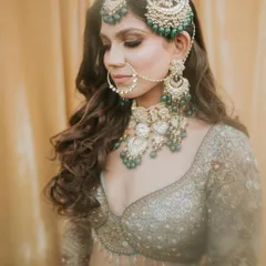A detailed shot of the bride's profile, focusing on her intricate jewelry and the soft, smokey eye makeup that complements the green stones.