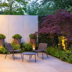 A modern patio designed for quiet contemplation. This space features a minimalist furniture set, large planters, and subtle uplighting against a feature wall, creating a chic and tranquil corner.