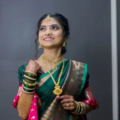An elegant portrait of a bride in a beautiful green and pink saree, looking up with a hopeful and happy expression.