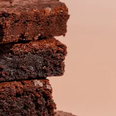 A close-up of our warm, fresh-baked brownies. They are perfectly gooey, fudgy, and decadent, designed to melt in your mouth.