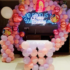 This Barbie-themed party setup features a balloon arch in shades of pink and peach. It's a simple yet elegant design perfect for a restaurant or home celebration.