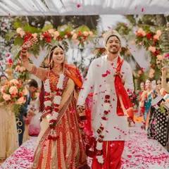 A joyous moment captured as the couple walks down the aisle after their wedding ceremony. The pathway is lined with flower petals, and the background shows the elegant floral arch and draped canopy of the mandap we designed.