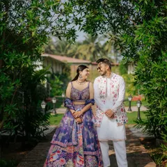 A full-length portrait of a couple in their stunning traditional outfits, framed by a natural arch of greenery at a Goa resort.