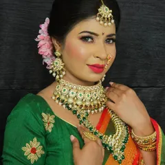 An elegant Maharashtrian look featuring a green and red Paithani saree. The makeup is classic, with defined eyes, a red lip, and a subtle bindi.