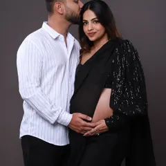 A tender moment captured in the studio. The dad-to-be kisses his partner's forehead as they both gently hold the baby bump, a beautiful pose that combines tradition with affection.