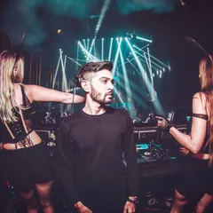 A shot from the booth, flanked by professional dancers under dramatic stage lighting. This reflects the high-production value and immersive experience of the events I headline.