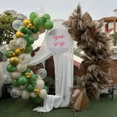 A chic and modern backdrop for a bridal shower, combining a bohemian pampas grass arch with a fun balloon garland in green, gold, and white.